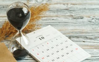 Hourglass with calendar on wooden desk close up